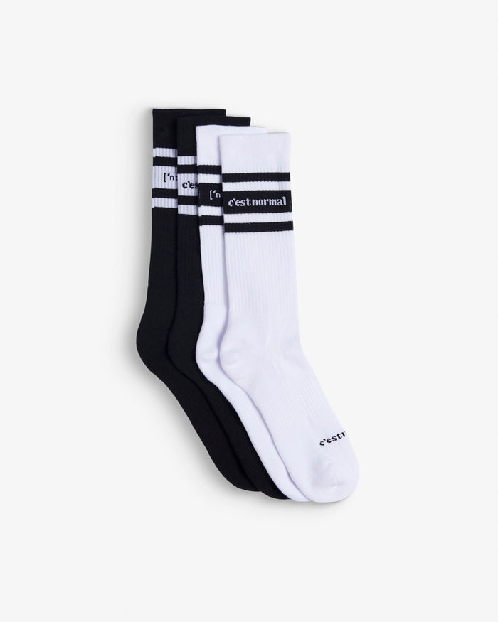 Two pairs of Les Socks laid flat on a white background, one in black and one in white. The image highlights the ribbed texture, contrasting stripes, and the c'est normal logo at mid-calf.