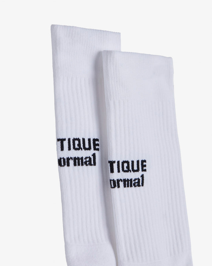 A close-up of a pair of white The Athlétique Socks, focusing on the ribbed texture and the black c'est normal logo stitched on the mid-calf.