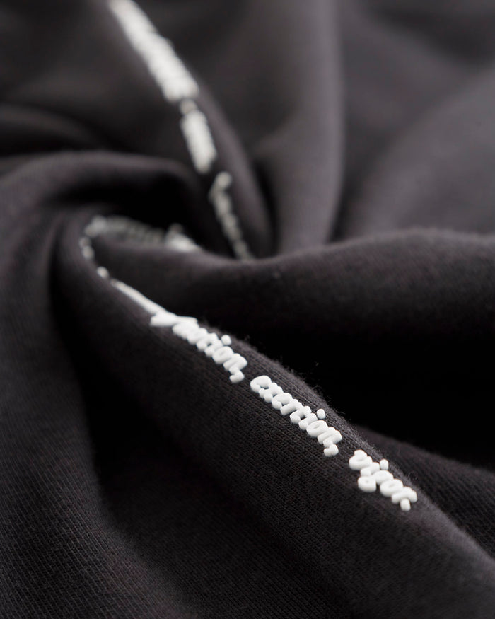 A detailed close-up of the black fabric on The Athlétique Tee, highlighting the white printed text reading 'action, exertion, vigor'.