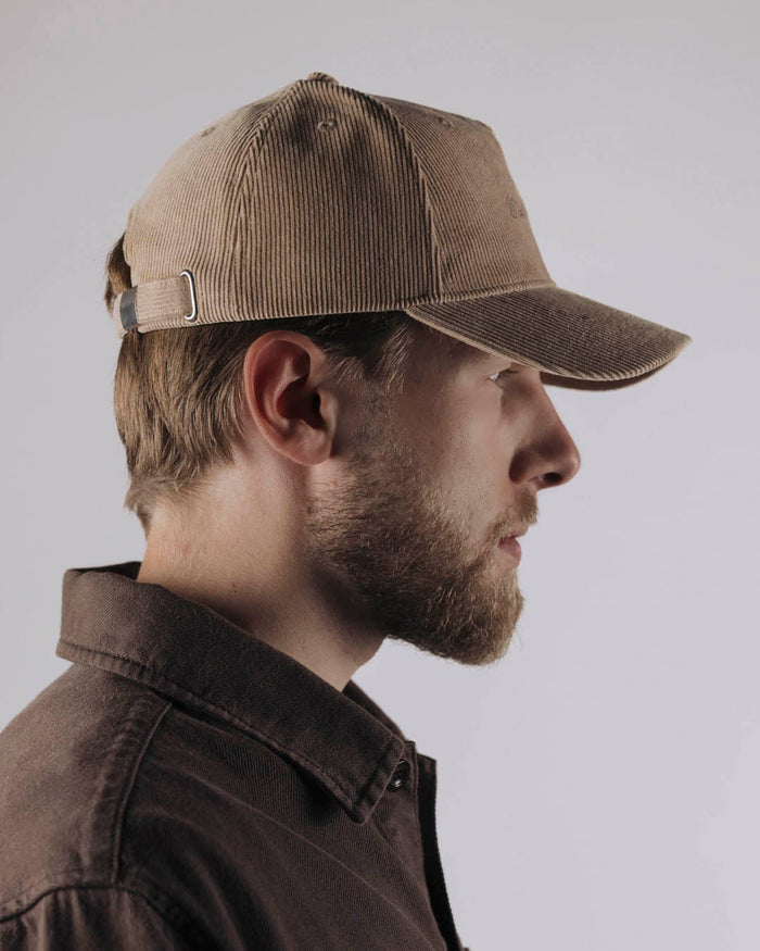 A side profile of a bearded man wearing The CÔTELÉ Corduroy Cap in Irish Cream and a brown shirt. The image highlights the cap's corduroy texture and the adjustable strap in the back.