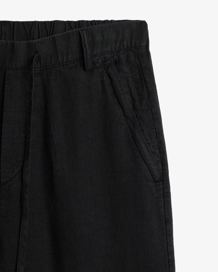The Holiday Linen Trouser in black — close-up of the waistband and tonal C'est normal embroidery
