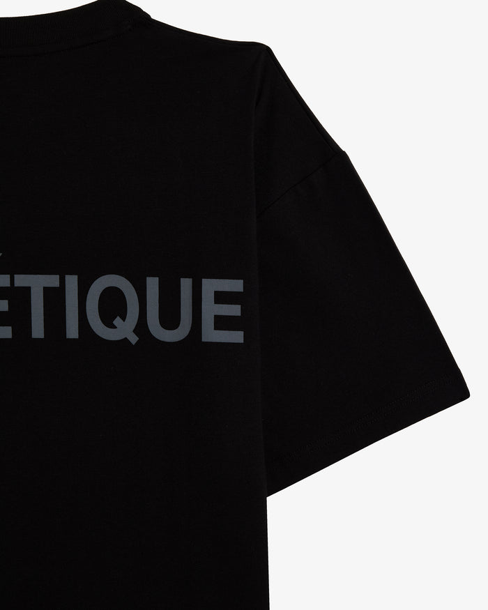 A close-up view of the back of The Oversized Gym T-Shirt in black, laid flat on a white background. The image highlights the grey Athlétique logo printed across the back.