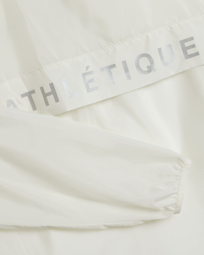A close-up detail of The Running Jacket in cream, highlighting the lightweight fabric, the sleeve's elastic cuff, and the reflective silver ATHLÉTIQUE text.