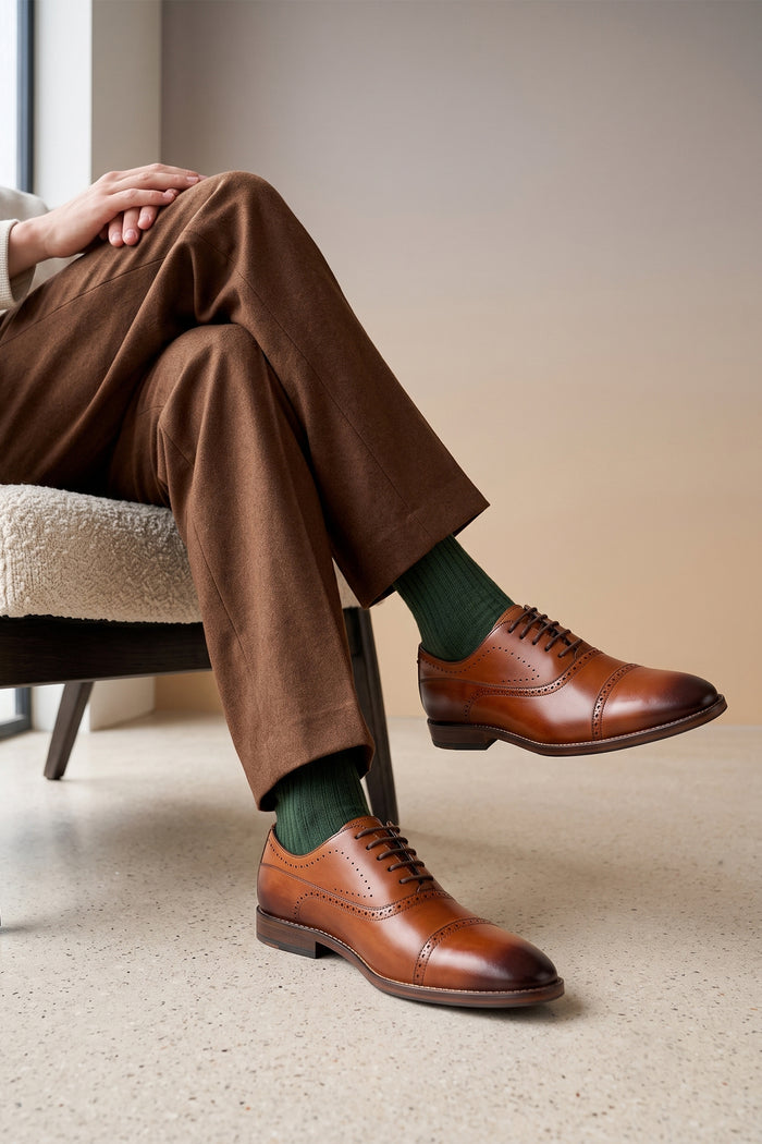 Man wearing Premium men's tan leather oxford shoes by Oswin Hyde London, featuring a cap toe with decorative perforations, closed lacing, contrast welt stitching, and a cushioned teal interior.