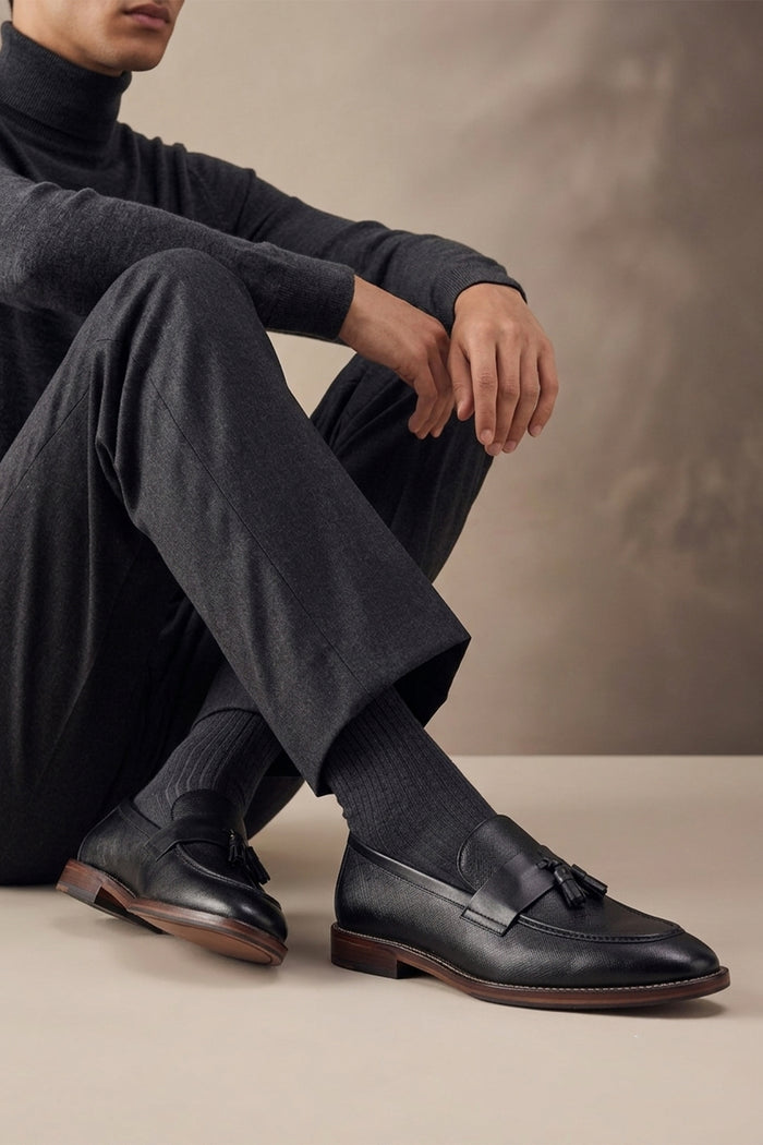 Man wearing Premium black leather tassel loafers for men featuring a textured finish, burnished moc-toe details, decorative leather tassels, and a cushioned teal interior.