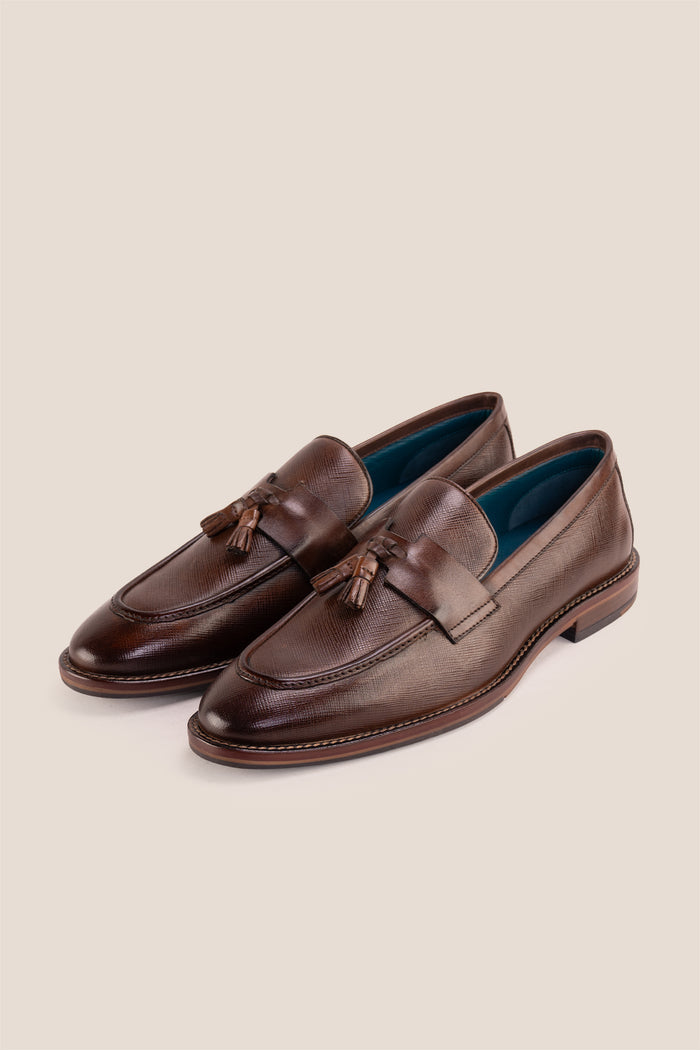 Premium brown leather tassel loafers for men featuring a textured finish, burnished moc-toe details, decorative leather tassels, and a cushioned teal interior.