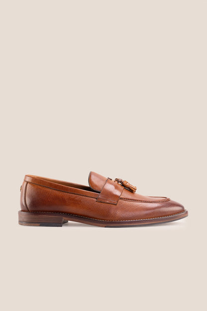 Premium tan leather tassel loafers for men featuring a textured finish, burnished moc-toe details, decorative leather tassels, and a cushioned teal interior.