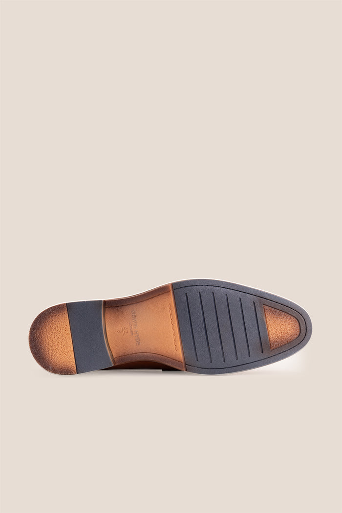Premium tan leather tassel loafers for men featuring a textured finish, burnished moc-toe details, decorative leather tassels, and a cushioned teal interior.