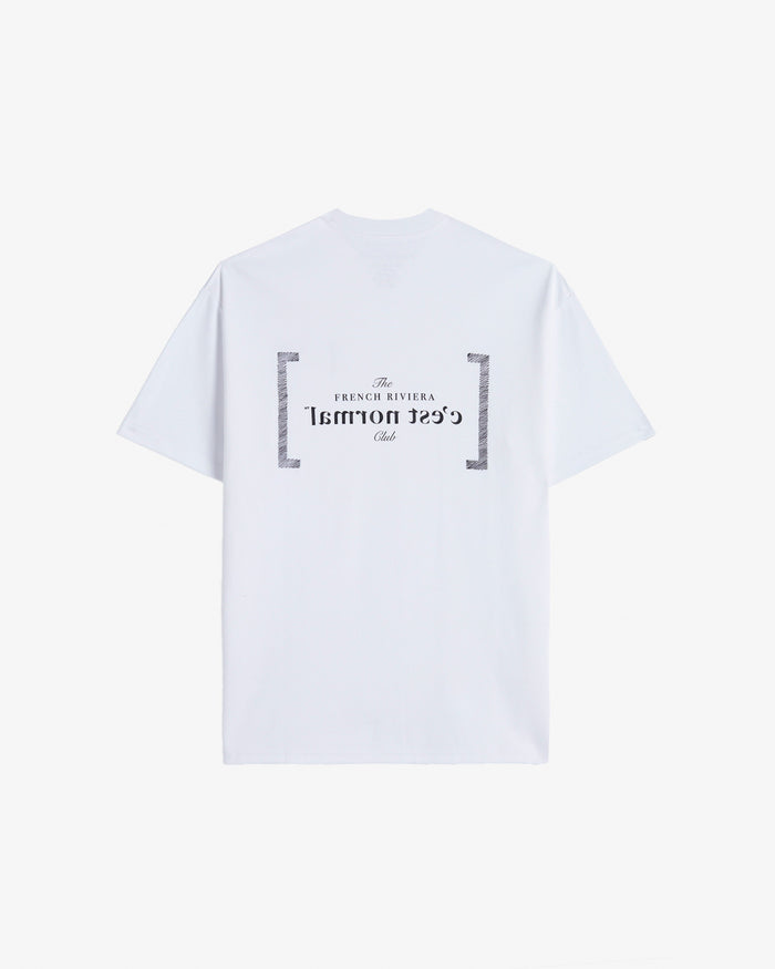 A back view of Le T-Shirt in white, laid flat on a white background. The image highlights the black FRC Edition mirror logo featuring the c'est normal text and The French Riviera Club.
