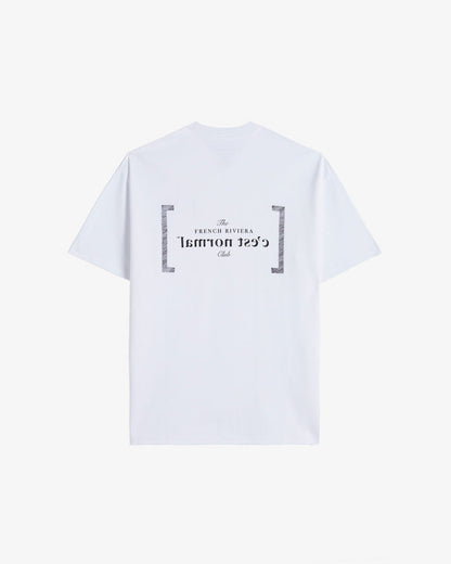 A back view of Le T-Shirt in white, laid flat on a white background. The image highlights the black FRC Edition mirror logo featuring the c'est normal text and The French Riviera Club.