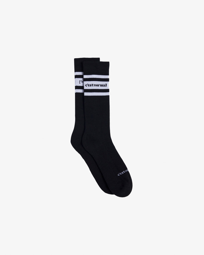 A pair of Les Socks in black, laid flat on a white background. The image highlights the white stripes and the c'est normal logo in contrast stitching at the mid-calf.