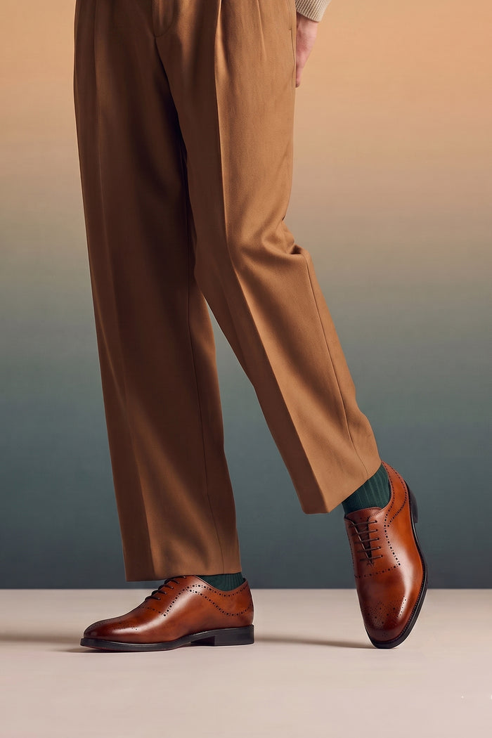 Model wearing Men’s Melton Oxford shoes in tan leather with classic closed lacing and elegant detailing, perfect for formal and refined dress codes.