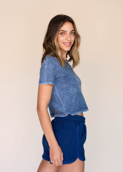 Woman wearing a blue top and shorts against a beige background