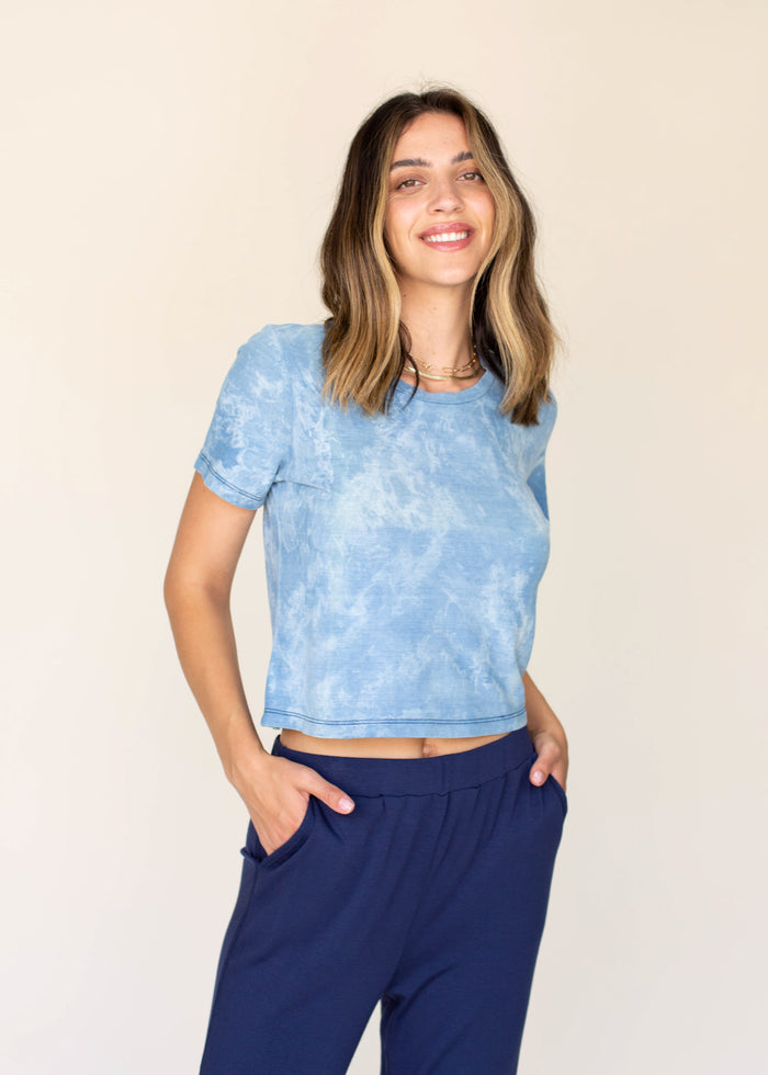 Woman wearing a blue and white tie-dye crop top and navy pants against a beige background