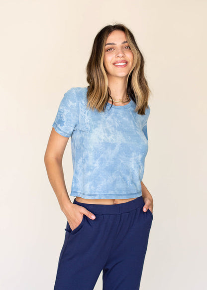 Woman wearing a blue and white tie-dye crop top and navy pants against a beige background