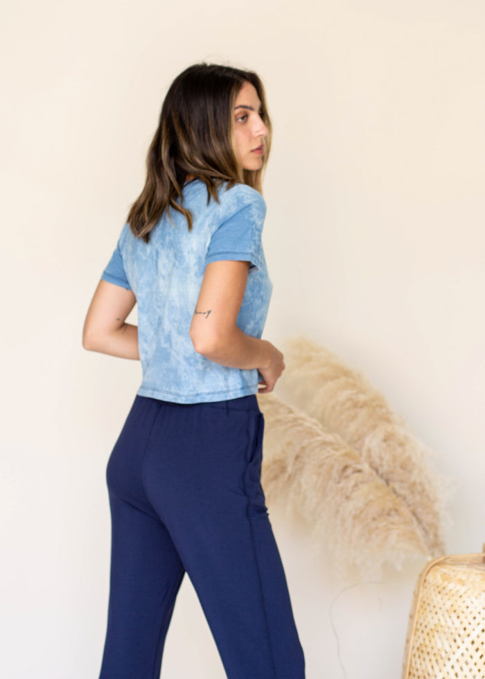 Woman wearing a blue and white tie dye top and navy pants against a beige background