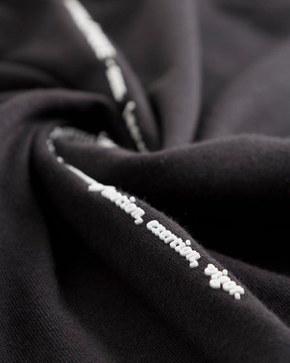 A detailed close-up of the black fabric on The Athlétique Tee, highlighting the white printed text reading 'action, exertion, vigor'.