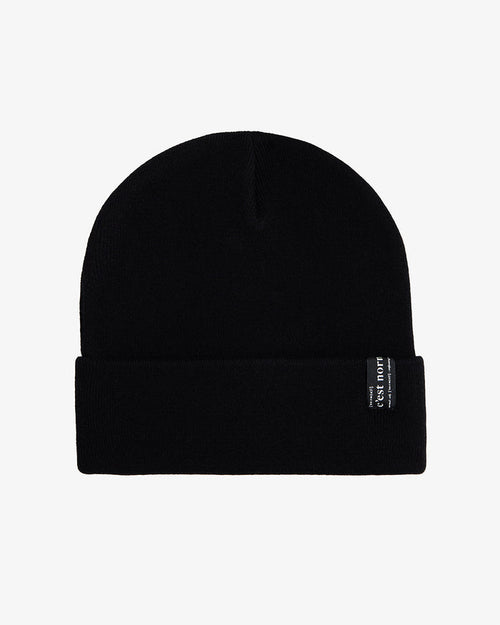 A front view of The Beanie in black, laid flat on a white background. The image highlights the fold-over cuff and the signature c'est normal label.