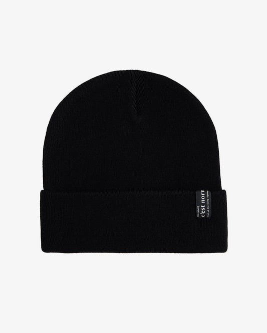 A front view of The Beanie in black, laid flat on a white background. The image highlights the fold-over cuff and the signature c'est normal label.