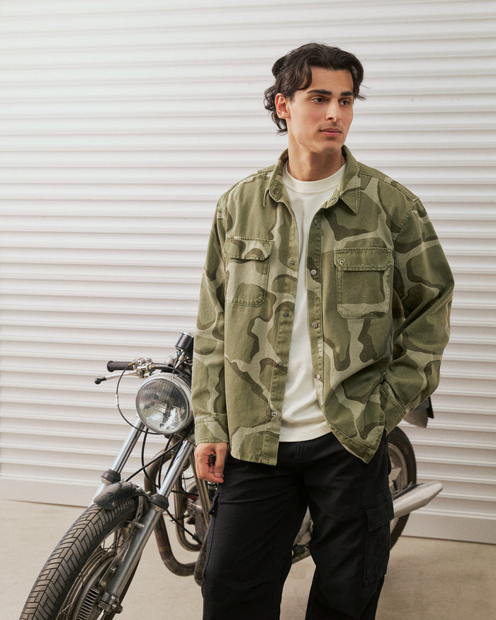 The Bilbao Overshirt in camo — worn while standing next to a vintage motorcycle