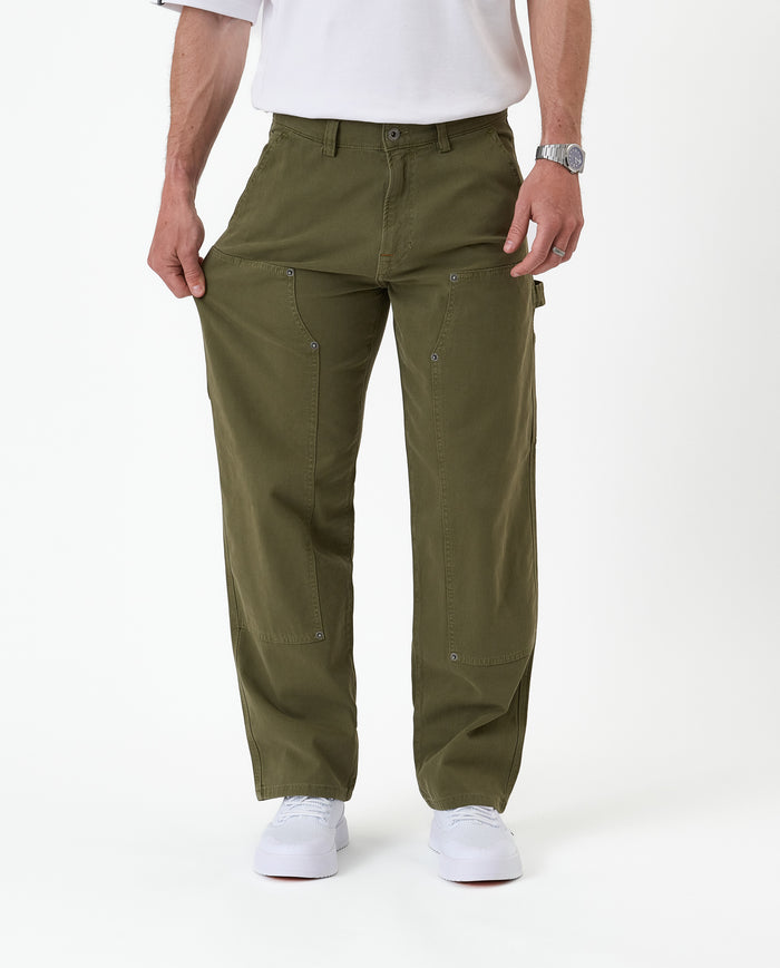 The Carpenter Pant in olive green — pulling the leg fabric to demonstrate the stretch material