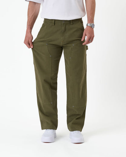 The Carpenter Pant in olive green — pulling the leg fabric to demonstrate the stretch material