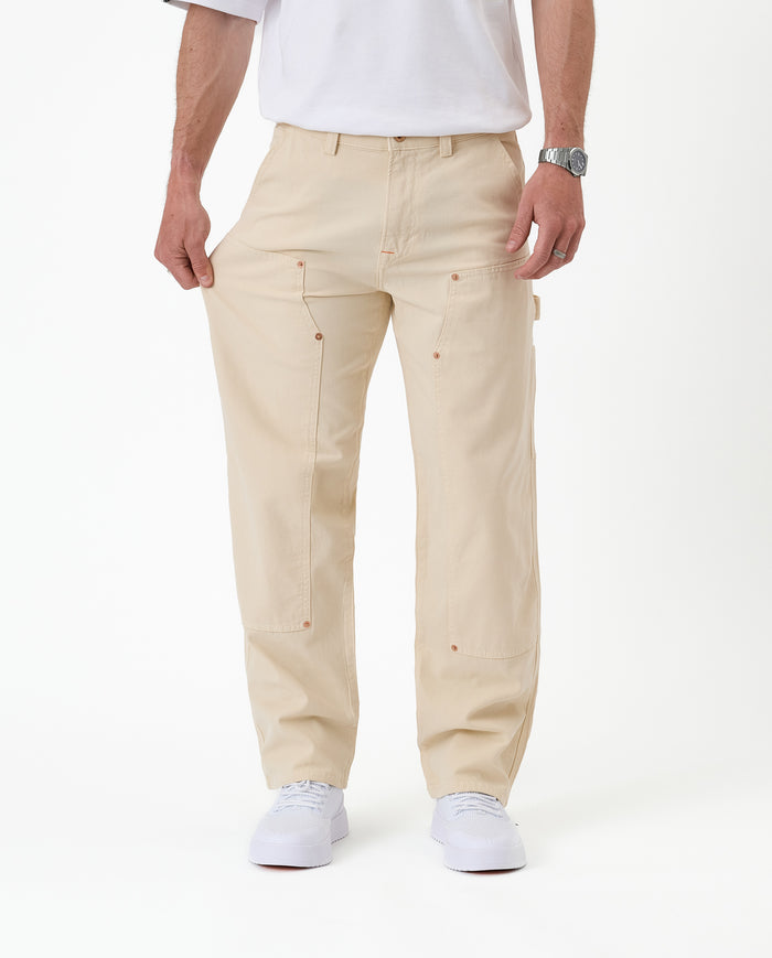 The Carpenter Pant in sand — pulled at the thigh to demonstrate the stretch fabric