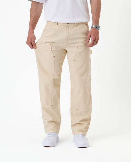 The Carpenter Pant in sand — pulled at the thigh to demonstrate the stretch fabric