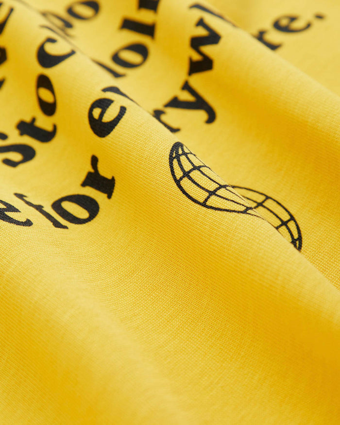 A detailed close-up of The c'est pari Oversized T-Shirt in yellow, focusing on the black screen-printed text and globe graphic on the back.