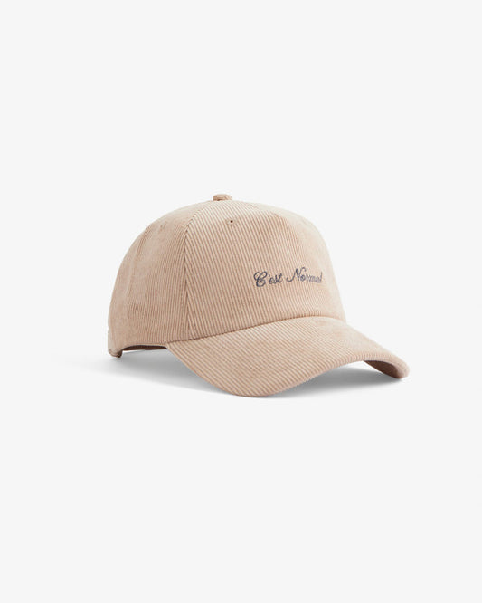 A side angle view of The CÔTELÉ Corduroy Cap in Irish Cream, laid flat on a white background. The image highlights the ribbed corduroy texture and the embroidered c'est normal logo on the front.