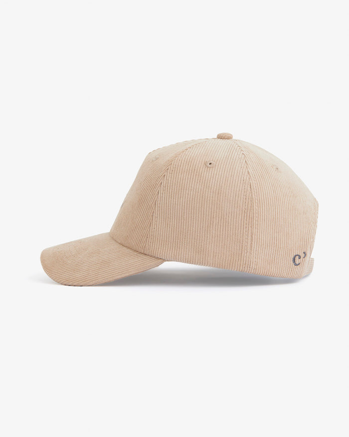 A side view of The CÔTELÉ Corduroy Cap in Irish Cream, laid flat on a white background. The image highlights the mid-wale corduroy texture and a small embroidered c'est normal logo near the back.
