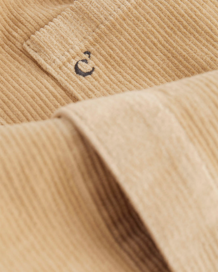 A close-up shot of the soft, corduroy fabric of The CÔTELÉ Corduroy Overshirt in Irish Cream, highlighting the c'est normal logo embroidered on the front.