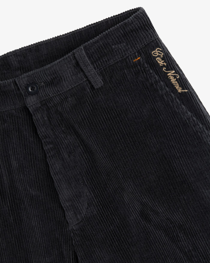 A close-up of The CÔTELÉ Corduroy Straight Pants in anthracite grey, focusing on the waistband, button closure, and the contrast embroidered c'est normal logo near the left hip.