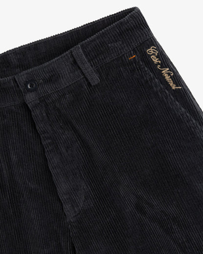 A close-up of The CÔTELÉ Corduroy Straight Pants in anthracite grey, focusing on the waistband, button closure, and the contrast embroidered c'est normal logo near the left hip.