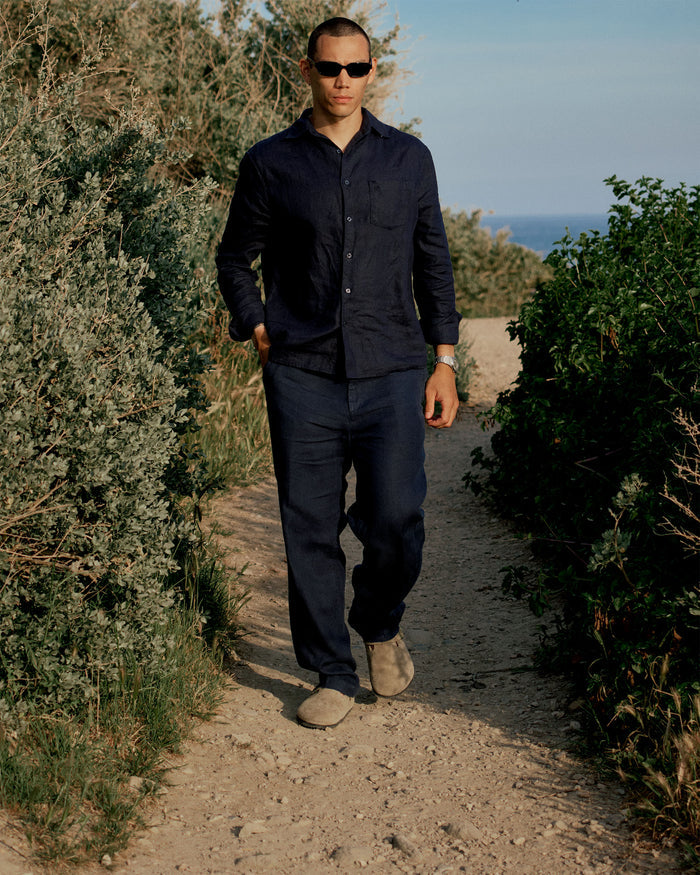 The Daily Linen Trouser in navy — worn while walking on a dirt path outdoors