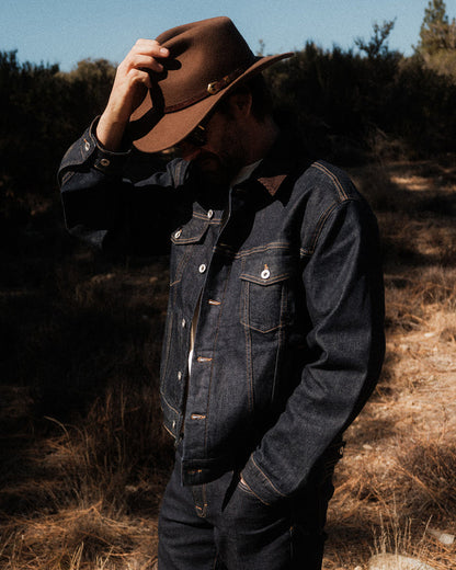 The Denim Jacket in dark indigo — worn outdoors with a brown hat