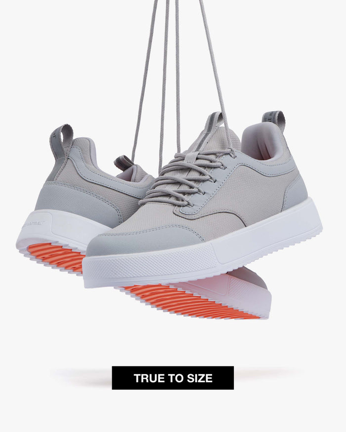 Two The Dynamic Waterproof Sneaker 2.0 Low in Grey/White Waterproof suspended by their laces against a white background. The image highlights the grey waterproof upper, white ultra lightweight EVA midsole, and original orange EVA rubber grid sole. A "TRUE TO SIZE" banner is visible at the bottom.