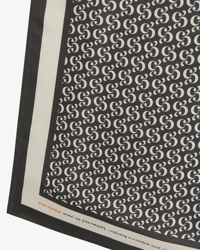 A detailed close-up of The Fall Bandana, showcasing the repeating black and cream monogram print. The image highlights the crisp contrast border with the c'est normal wordmark and definition detail.