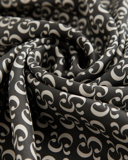 A close-up view of the lightweight woven fabric of The Fall Bandana, showcasing the signature repeating c'est normal monogram print in black and cream.