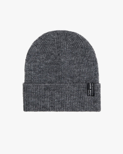 The Hairy Beanie in charcoal, laid flat on a white background. The image highlights the soft, fuzzy texture of the knit material and the black tag with the c'est normal logo on the brim.
