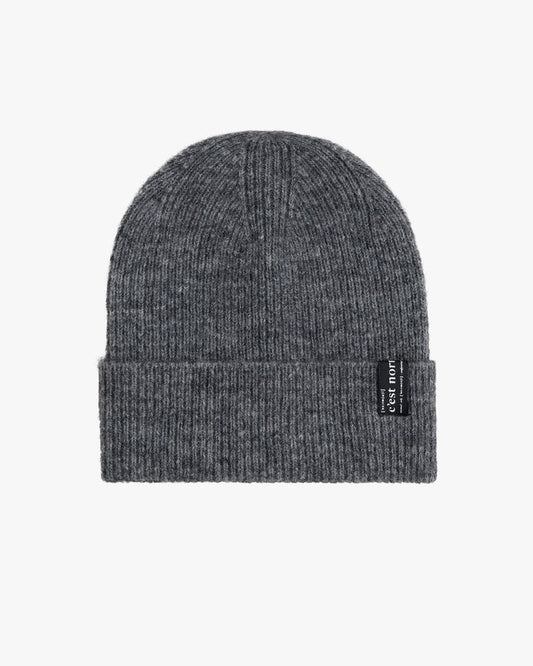 The Hairy Beanie in charcoal, laid flat on a white background. The image highlights the soft, fuzzy texture of the knit material and the black tag with the c'est normal logo on the brim.