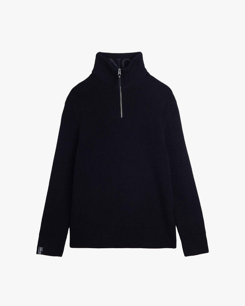 A front view of The Halfzip Sweater in black, laid flat on a white background. The image highlights the standing collar with a metal zipper, the structured knit material, and the c'est normal cuff tag on the right sleeve.