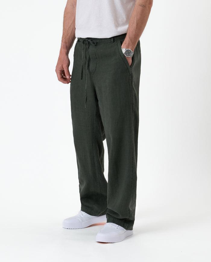 The Holiday Linen Trouser in dark khaki — worn with white sneakers