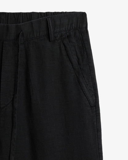 The Holiday Linen Trouser in black — close-up of the waistband and tonal C'est normal embroidery