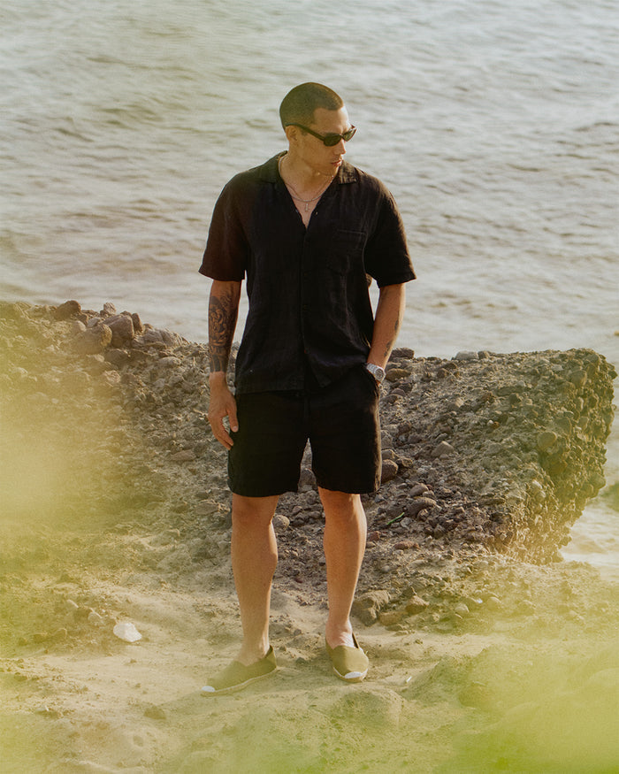 The Holiday Linen Short in black — worn with a matching linen shirt by the sea