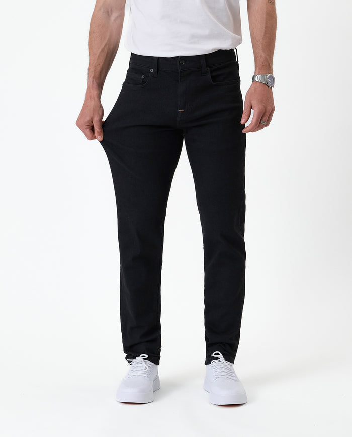 The Jeans Slim Fit in jet black — pulling the fabric to demonstrate the Motion Fabric stretch