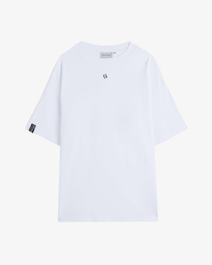 A front view of The Première T-Shirt in white, laid flat on a white background. The image highlights the oversized fit, ribbed crewneck, small central logo, and the signature c'est normal cuff tag on the right sleeve.