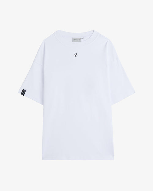 A front view of The Première T-Shirt in white, laid flat on a white background. The image highlights the oversized fit, ribbed crewneck, small central logo, and the signature c'est normal cuff tag on the right sleeve.