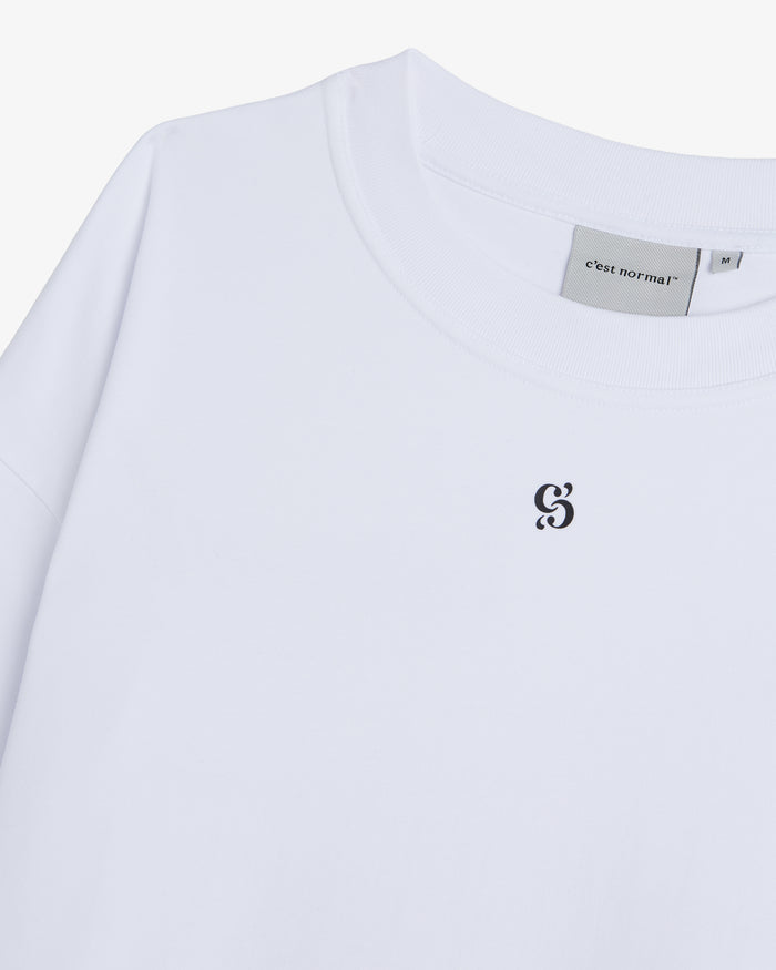 A detailed close-up of The Première T-Shirt in white, focusing on the ribbed crewneck collar, the inside neck tag, and the small black c'est normal logo printed on the chest.