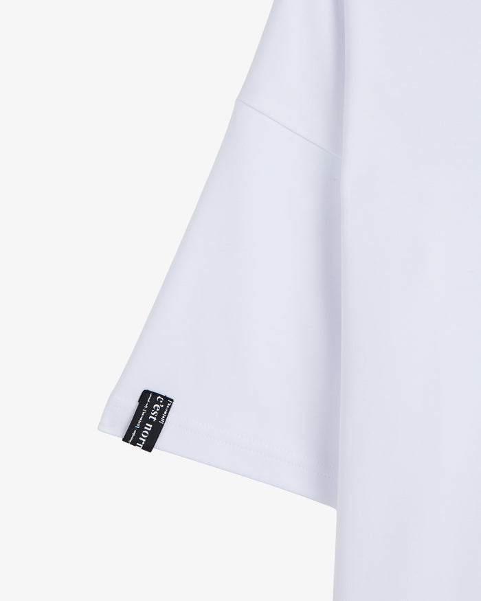 A close-up shot of the right sleeve of The Première T-Shirt in white, highlighting the signature black cuff tag with the white c'est normal logo.